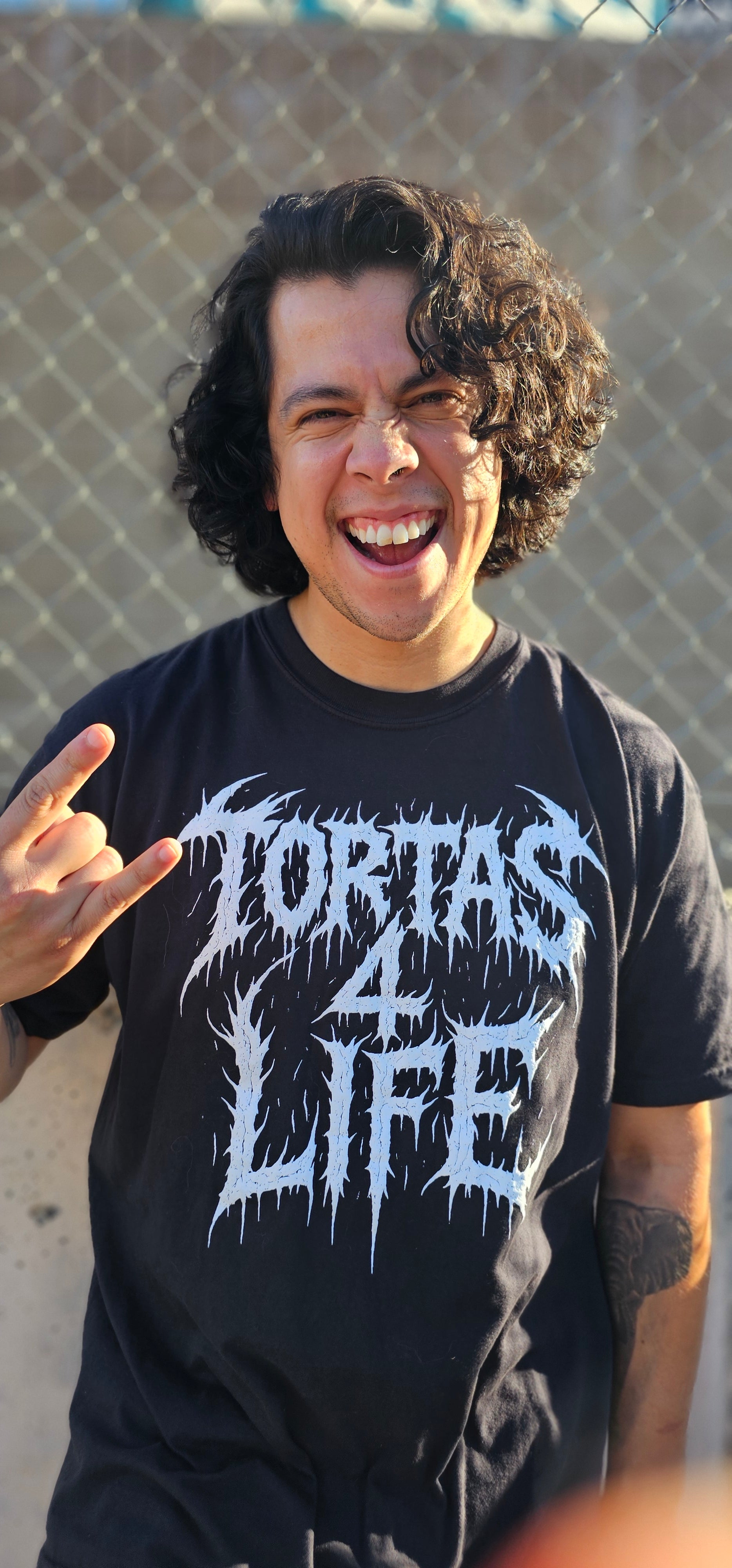 Person wearing a black t-shirt with white text and graphics, standing against a textured wall.